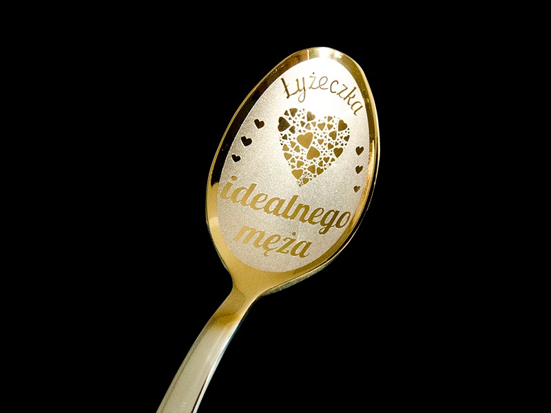 Złota łyżeczka z grawerem 'Łyżeczka idealnego męża' oraz motywem serca z mniejszych serduszek na czarnym tle.