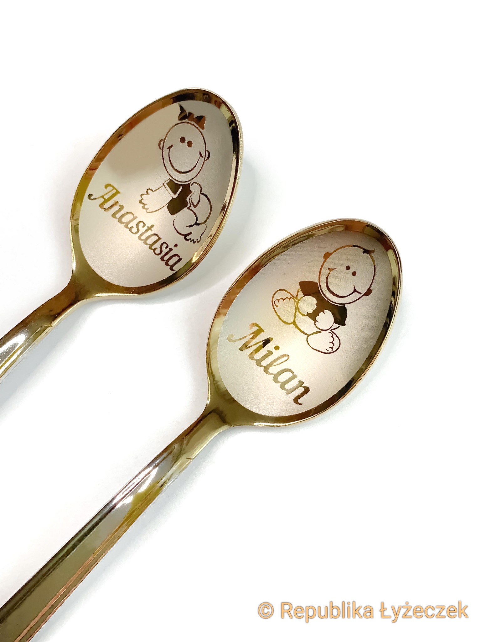 Dwie złote łyżeczki z wygrawerowanymi imionami 'Anastasia' i 'Milan' oraz rysunkami dzieci na białym tle.