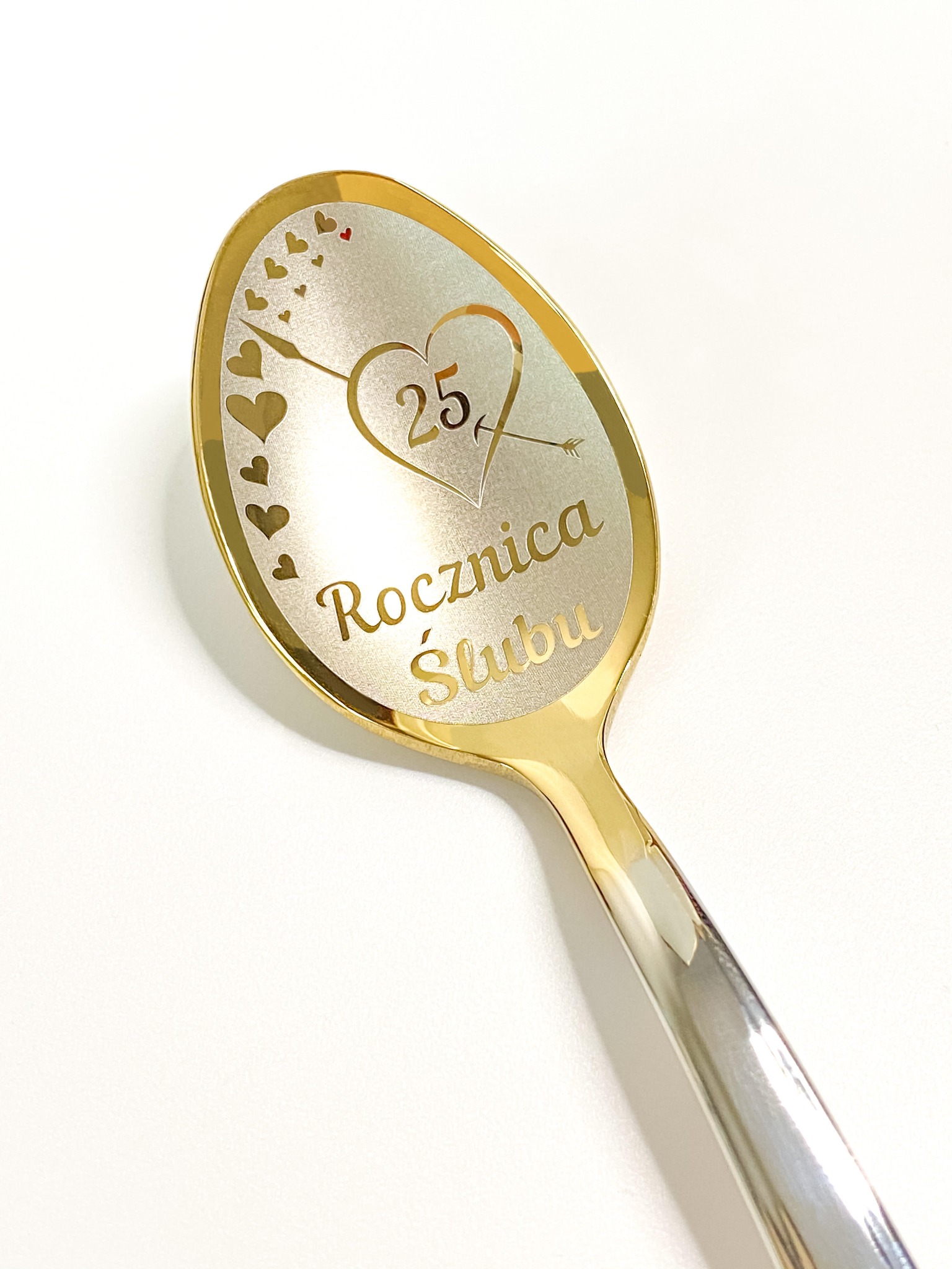 Pamiątkowa, złoto-srebrna łyżeczka z grawerem '25 Rocznica Ślubu' i motywem serc, leżąca na białym tle.