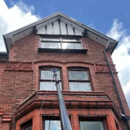 Ceglana fasada budynku z wysuwaną lancą do czyszczenia okien, widok z dołu na tle błękitnego nieba z chmurami.