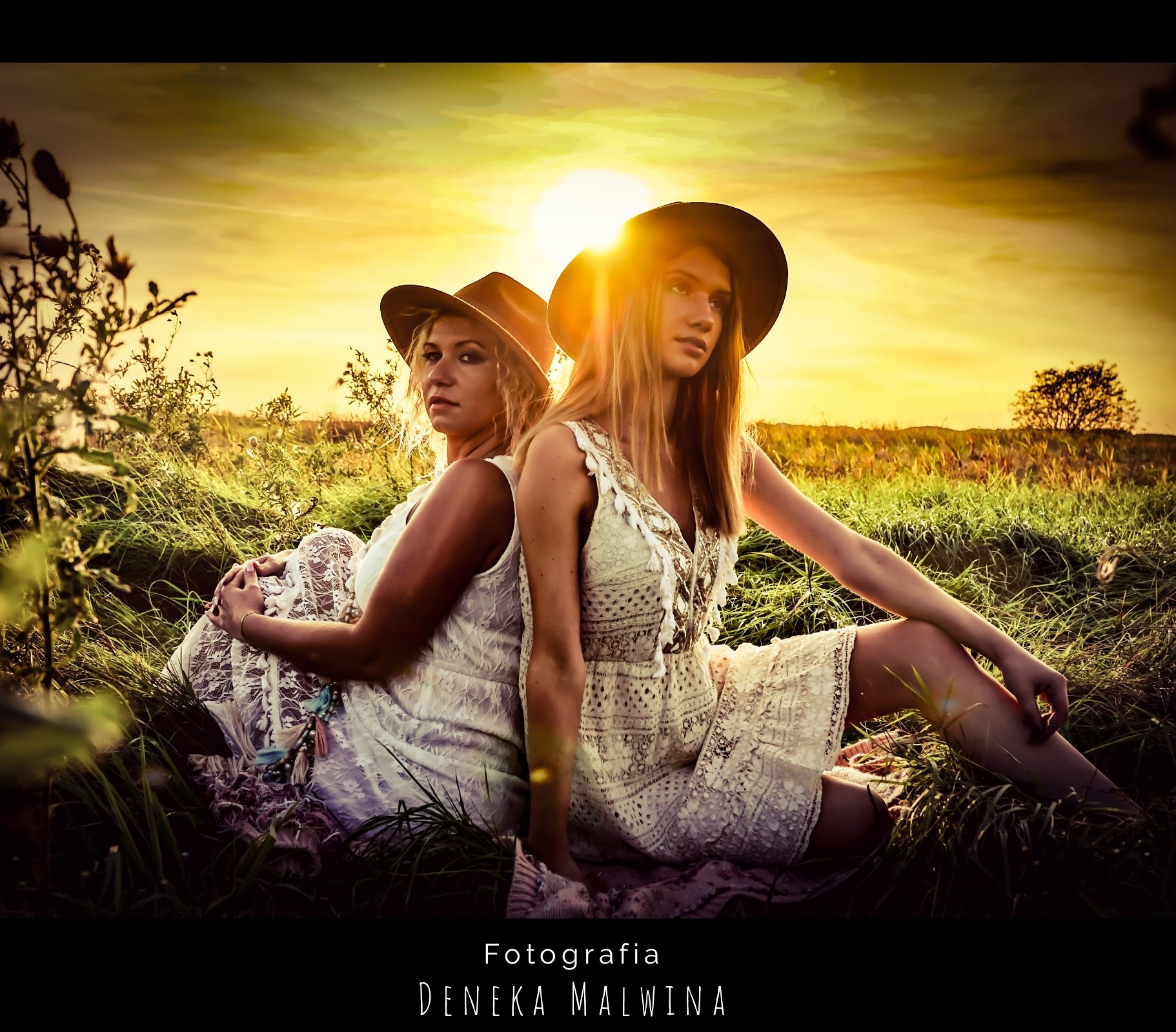 Dwie kobiety w białych, koronkowych sukienkach i kapeluszach siedzą plecami do siebie na łące o zachodzie słońca.