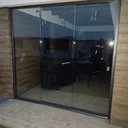 Przesuwne, szklane drzwi tarasowe z czarną ramą, widok na wnętrze z grillem i schodami, ślady na tarasie.