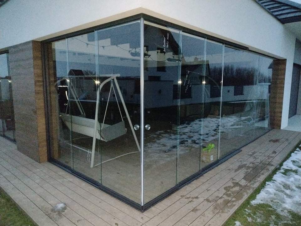 Szklana zabudowa tarasu z aluminiowymi ramami, widok z zewnątrz na drewniany taras i huśtawkę wewnątrz, częściowo pokryty śniegiem.