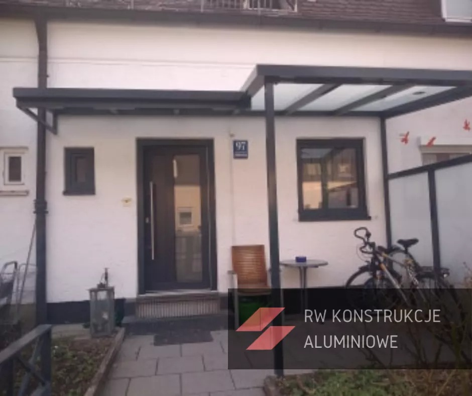 Nowoczesna, grafitowa konstrukcja z zadaszeniem nad wejściem do domu, z numerem 97, obok okna i roweru, widoczny lampion i krzesło.