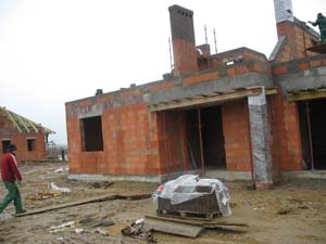 Wznoszenie ścian zewnętrznych z czerwonej cegły dziurawki na budowie parterowego domu jednorodzinnego w trakcie realizacji, widoczne szalunki nad otworami okiennymi i drzwiowymi, komin w surowym...