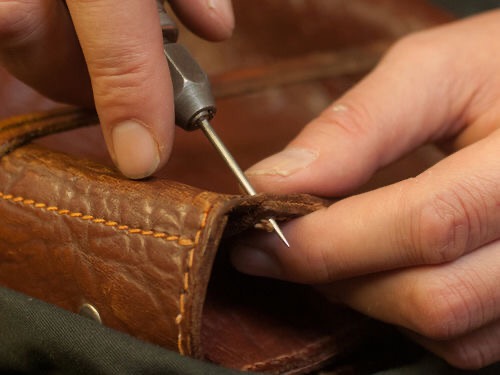 Ręczne zszywanie brązowej skórzanej torby za pomocą szydła i pomarańczowej nici.