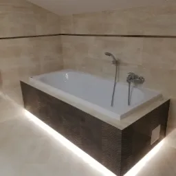 Nowoczesna wanna obudowana płytkami z motywem fali, podświetlona listwą LED w łazience wykończonej beżowymi płytkami.