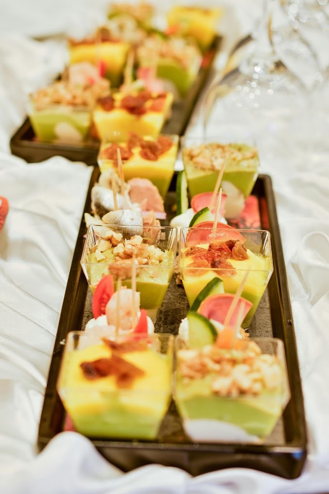 Elegancko podane desery w małych, przezroczystych naczyniach na czarnej tacy, dekorowane owocami, ziołami i orzechami, na białym obrusie.