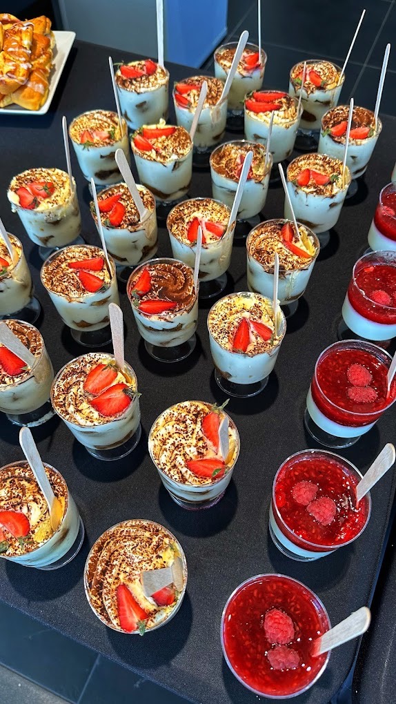 Deserowe kompozycje w szklanych naczyniach: tiramisu z truskawkami i deser malinowy na czarnym tle, z drewnianymi łyżeczkami. Elegancki catering na imprezę.