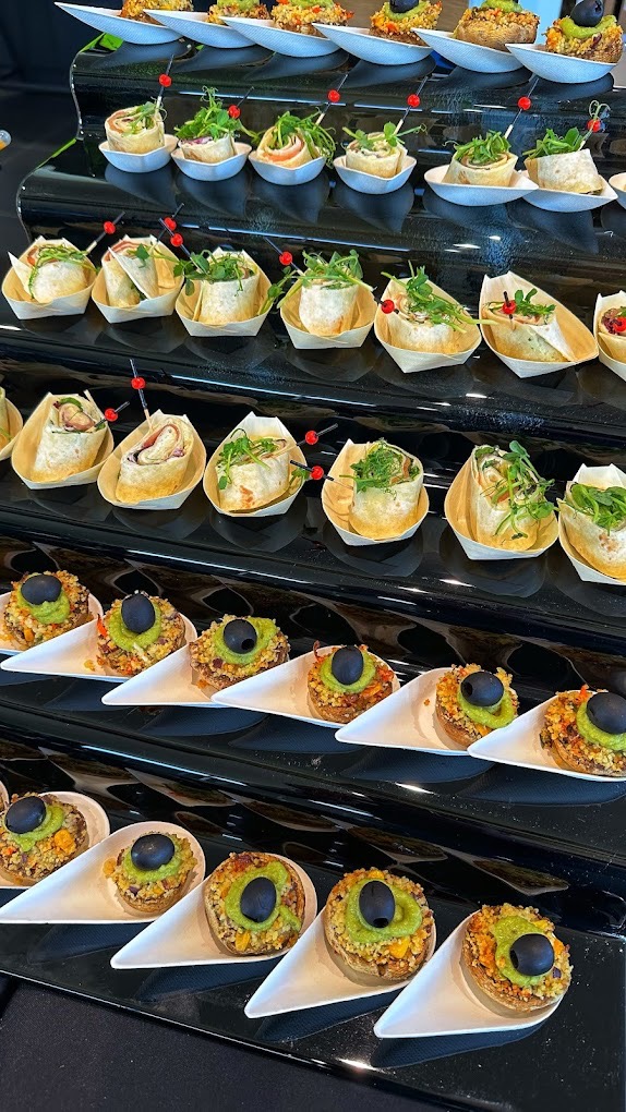 Elegancki catering: wielopoziomowa ekspozycja przekąsek na przyjęciu. Wrapy z zieleniną i mini tartaletki z oliwkami na czarnym, błyszczącym stojaku.