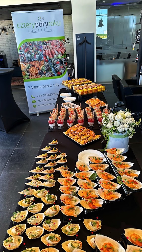 Stół cateringowy z różnorodnymi przekąskami, roll-upem reklamowym firmy 'Cztery Pory Roku Catering' w tle, eleganckie wnętrze.