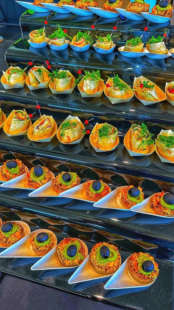 Elegancki catering: Rzędy mini przekąsek na czarnym, lustrzanym stojaku. Roladki z warzywami i pastami, koreczki z ziołami i oliwkami, podane w oryginalnych naczyniach.