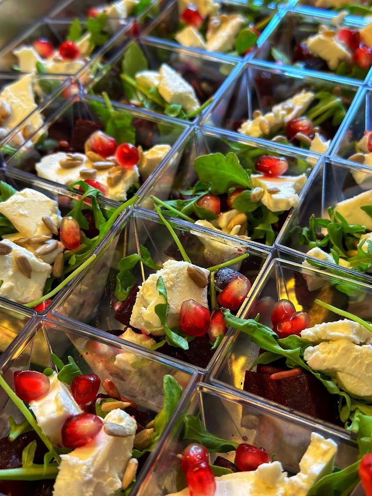 Przekąski w przezroczystych pojemnikach: burak, ser, rukola, granat, słonecznik. Elegancki catering na przyjęcie, widok z góry, ostre światło.