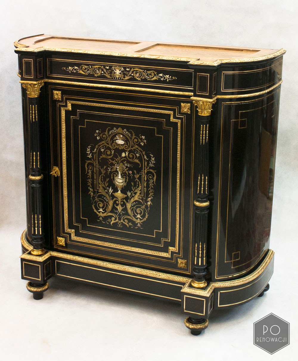 Czarna komoda w stylu Ludwika XVI z intarsjami i złoceniami, widoczne detale kolumnowe i dekoracyjne ornamenty.