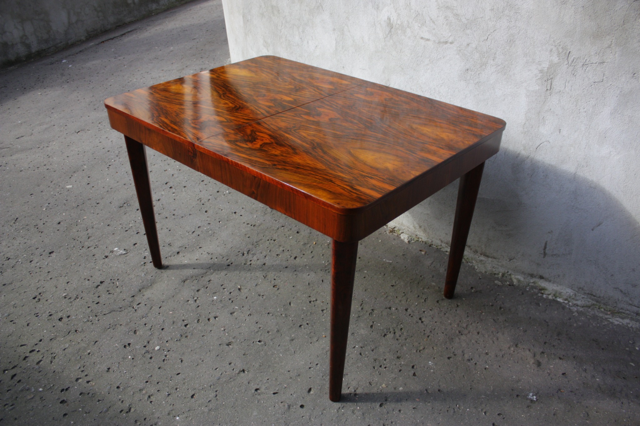 Stół z fornirem o bogatym, ciemnym rysunku drewna, wykonany w Warszawie. Widoczne połączenie dwóch części blatu.