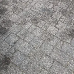 Szara kostka brukowa ułożona w regularny wzór, widoczne delikatne plamy i zabrudzenia na powierzchni.