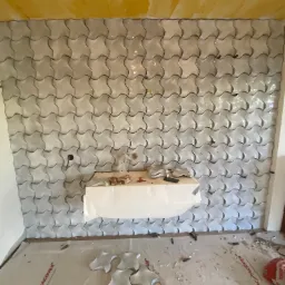 Układanie mozaiki w kształcie czterolistnej koniczyny na ścianie w Elblągu, widoczne narzędzia i zapas płytek, sufit po malowaniu.