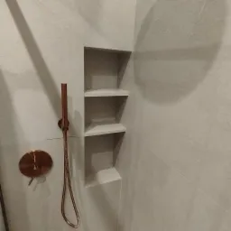 Szare płytki w łazience z wnęką z trzema półkami i miedzianą armaturą prysznicową.