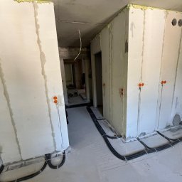 BoWe Energy Jakub Mucha - Wnętrze w trakcie prac elektrycznych: kable w peszlach ułożone na podłodze, puszki elektryczne w ścianach, surowy stan wykończenia.