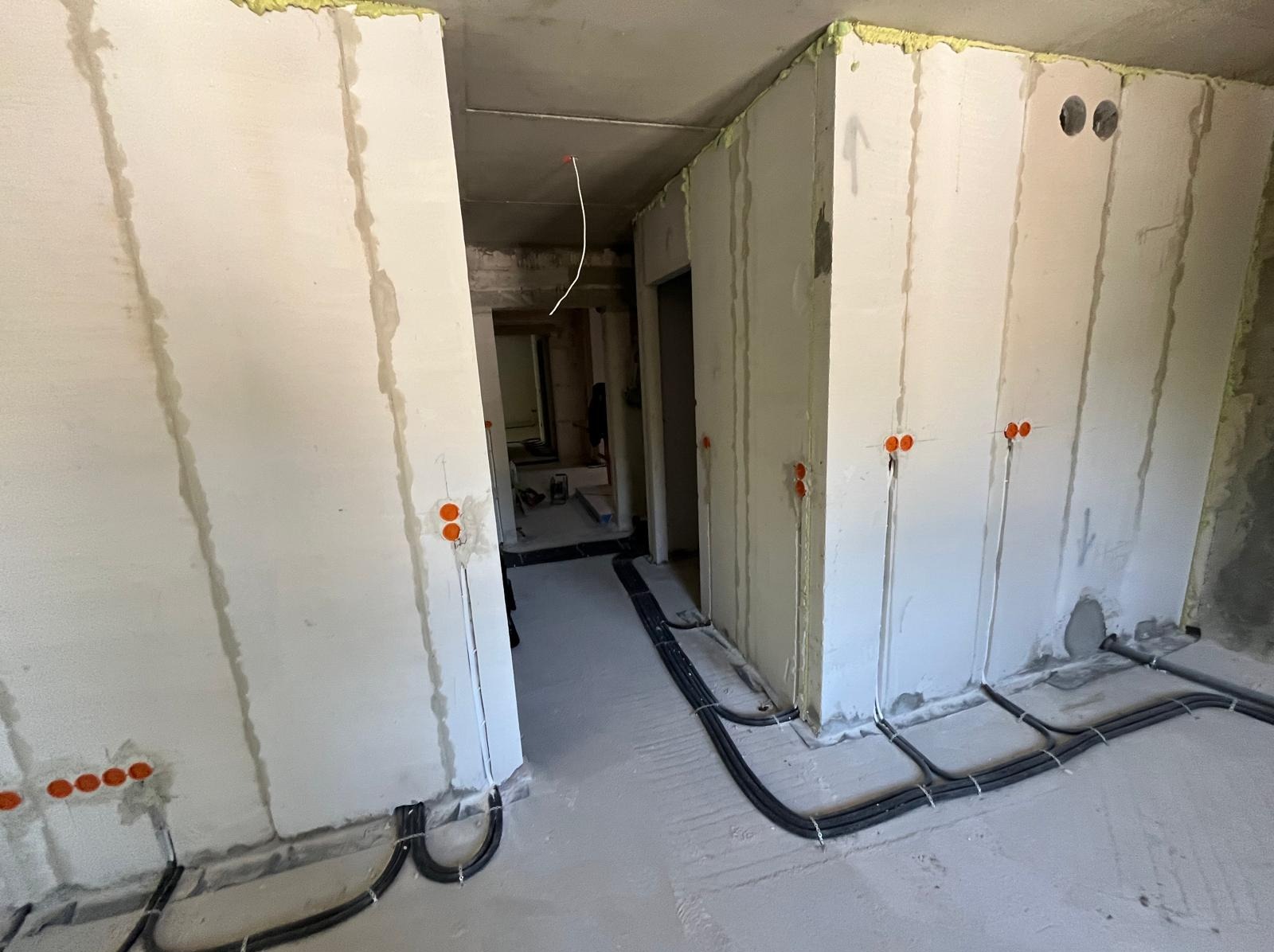 Wnętrze w trakcie prac elektrycznych: kable w peszlach ułożone na podłodze, puszki elektryczne w ścianach, surowy stan wykończenia.