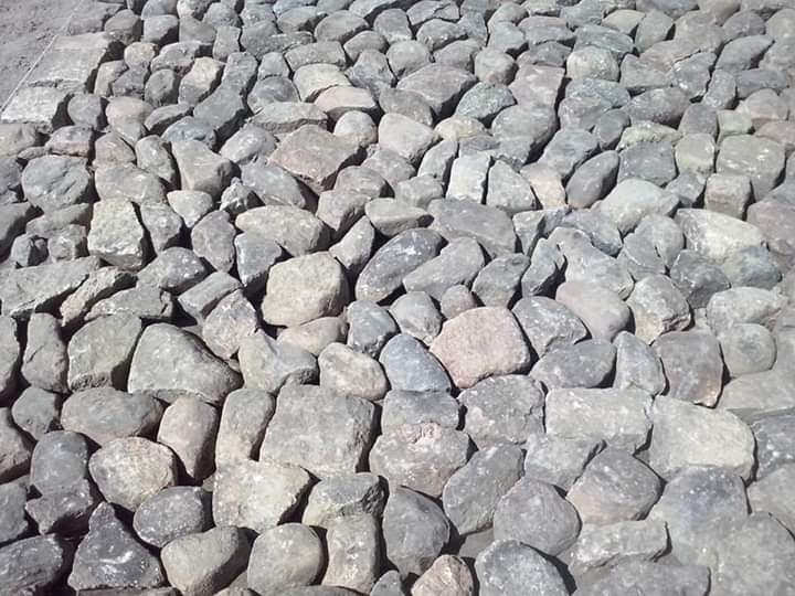 Nierówna powierzchnia wyłożona szarymi kamieniami o nieregularnych kształtach, widoczne szczeliny między kamieniami, fragment krawężnika w tle.