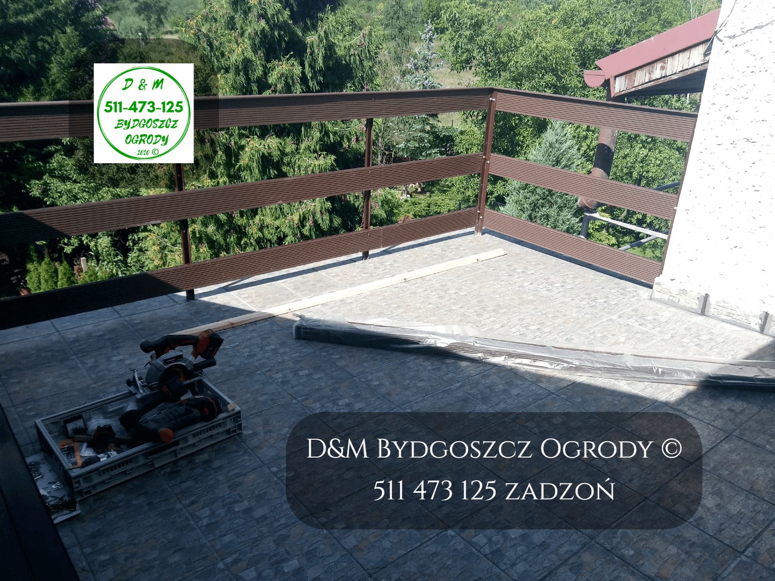 Montaż brązowego ogrodzenia z desek kompozytowych na tarasie, widoczna piła do cięcia i materiały budowlane, w tle zieleń drzew.