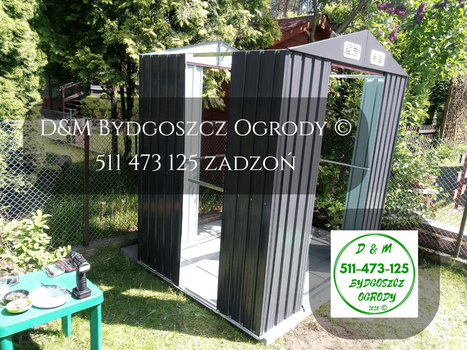 Montaż szarej, metalowej konstrukcji szopy ogrodowej w trakcie realizacji, widoczne narzędzia na zielonym stoliku, logo firmy w prawym dolnym rogu zdjęcia.