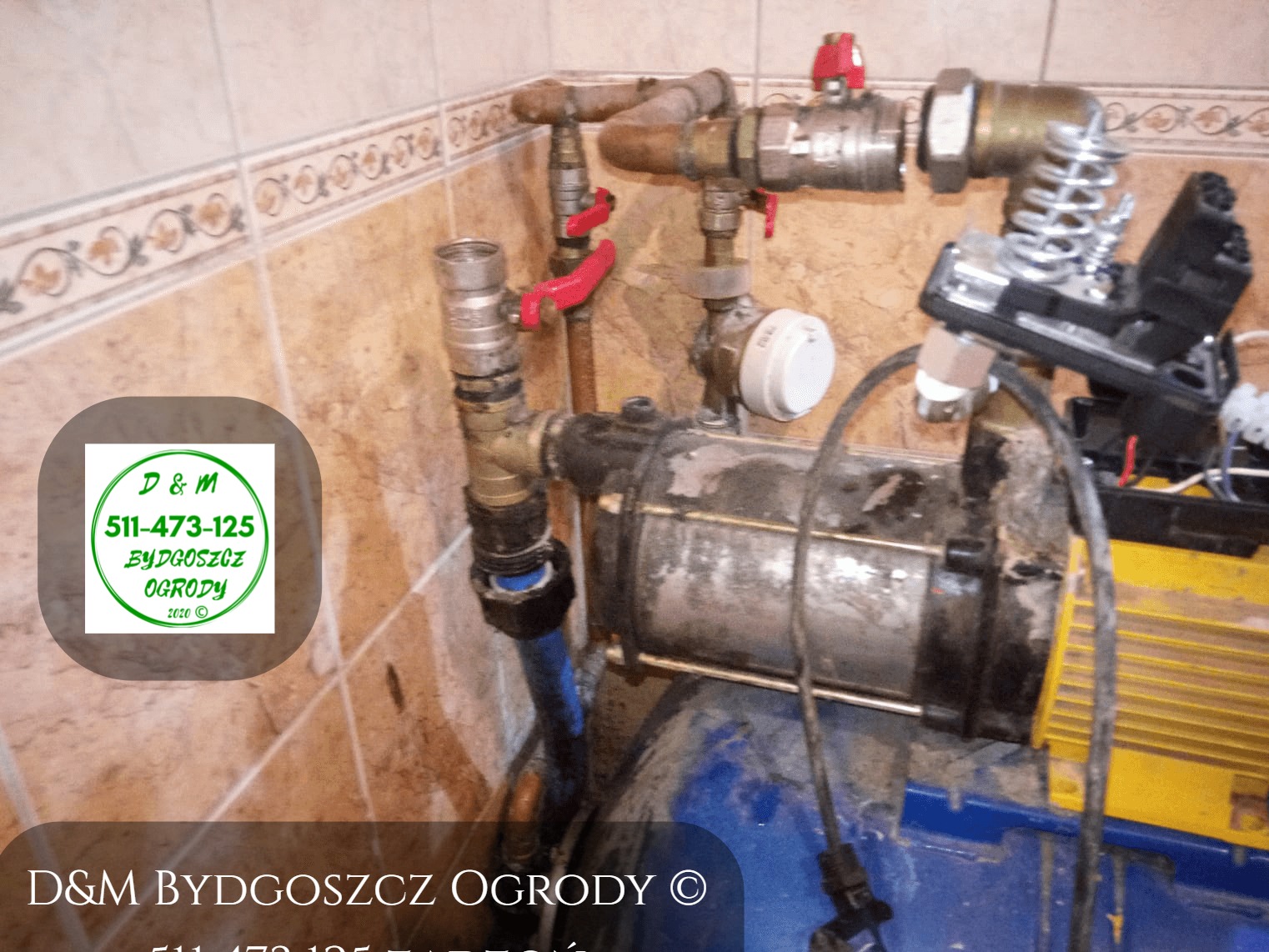 Brudny hydrofor z żółtym silnikiem, widoczne rury, zawory i biały presostat, zamontowany w pomieszczeniu z brązowymi płytkami. Na zdjęciu widoczne logo firmy D&M Bydgoszcz Ogrody.