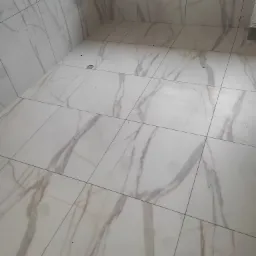 Wykończona łazienka z białymi płytkami imitującymi marmur na podłodze i ścianach, widoczne wystające rury instalacji wodnej.