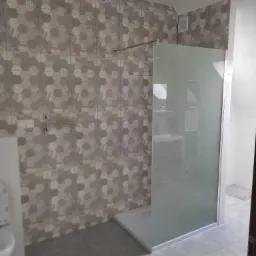 Wykończona łazienka z kabiną prysznicową typu walk-in, szare heksagonalne płytki na ścianie, szara podłoga, widoczne oświetlenie sufitowe.