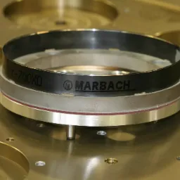 Precyzyjny, wieloelementowy pierścień z logo Marbach, zamocowany na metalowej płycie z otworami, widoczne oznaczenie 'ker-700XD'.