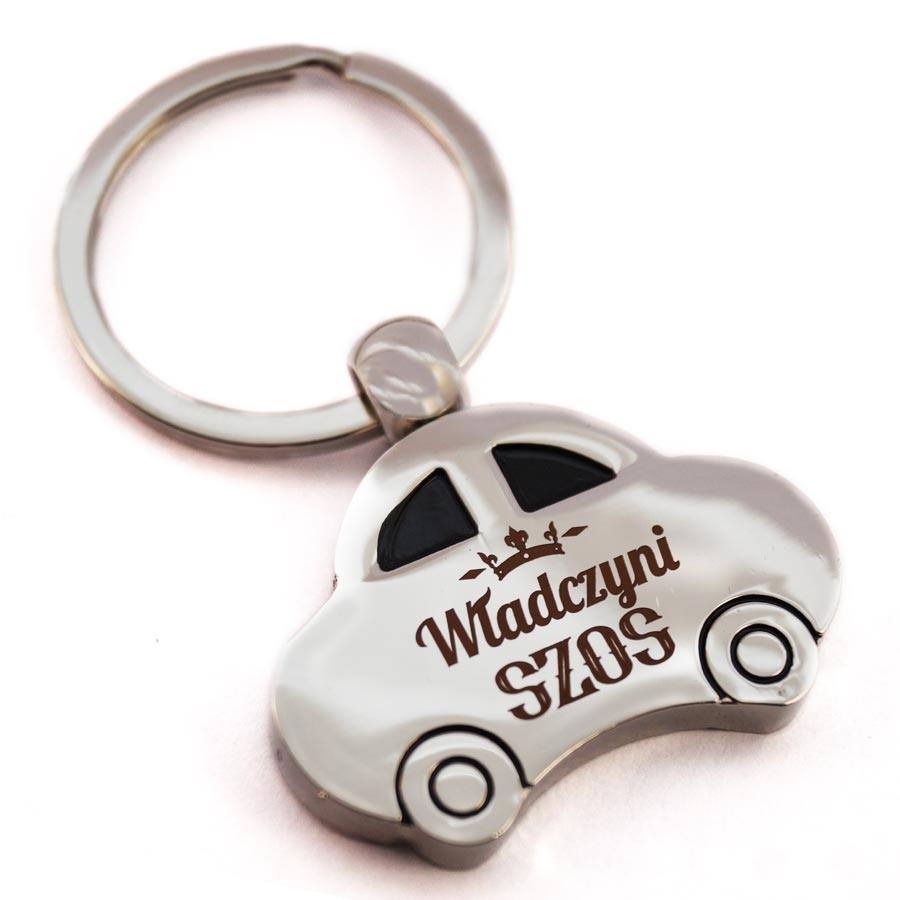 Brelok w kształcie srebrnego samochodu z napisem 'Władczyni Szos' w brązowej czcionce, zawieszony na metalowym kółku.