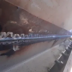 Metalowa konstrukcja z widocznym spoiwem po spawaniu, z rzędem śrub po prawej stronie, widok z dołu pod kątem.