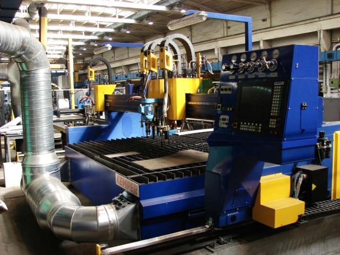 Duża, niebiesko-żółta maszyna CNC do cięcia metalu w hali produkcyjnej w Kleczewie, z systemem odciągu spalin z rur ze stali nierdzewnej.