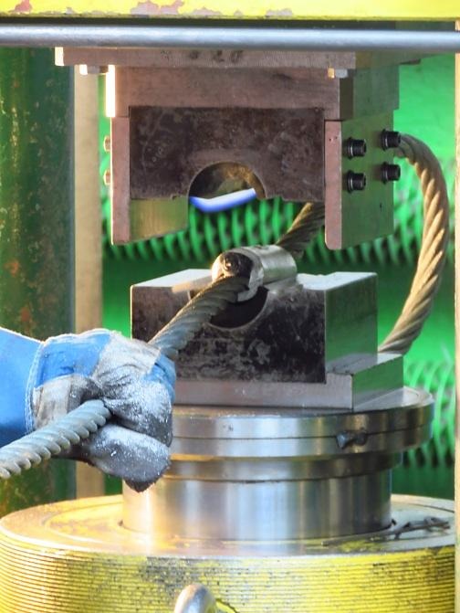 Pracownik w rękawicy umieszcza grubą linę stalową w zaciskarce hydraulicznej podczas prac ziemnych.