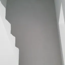 Surowa, szara ściana w trakcie prac wykończeniowych, widoczne białe schody z surowego betonu, niedokończone krawędzie i nier&oacute;wności na ścianie.