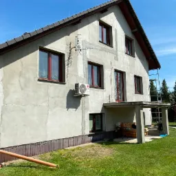 Dom jednorodzinny w trakcie prac wykończeniowych elewacji, widoczne ślady po łatach, w tle rusztowanie, błękitne niebo.