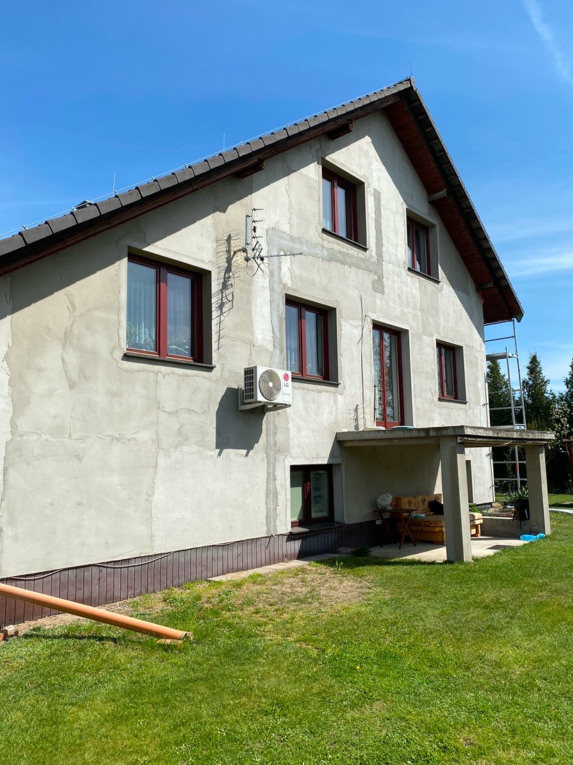 Dom jednorodzinny w trakcie prac wykończeniowych elewacji, widoczne ślady po łatach, w tle rusztowanie, błękitne niebo.