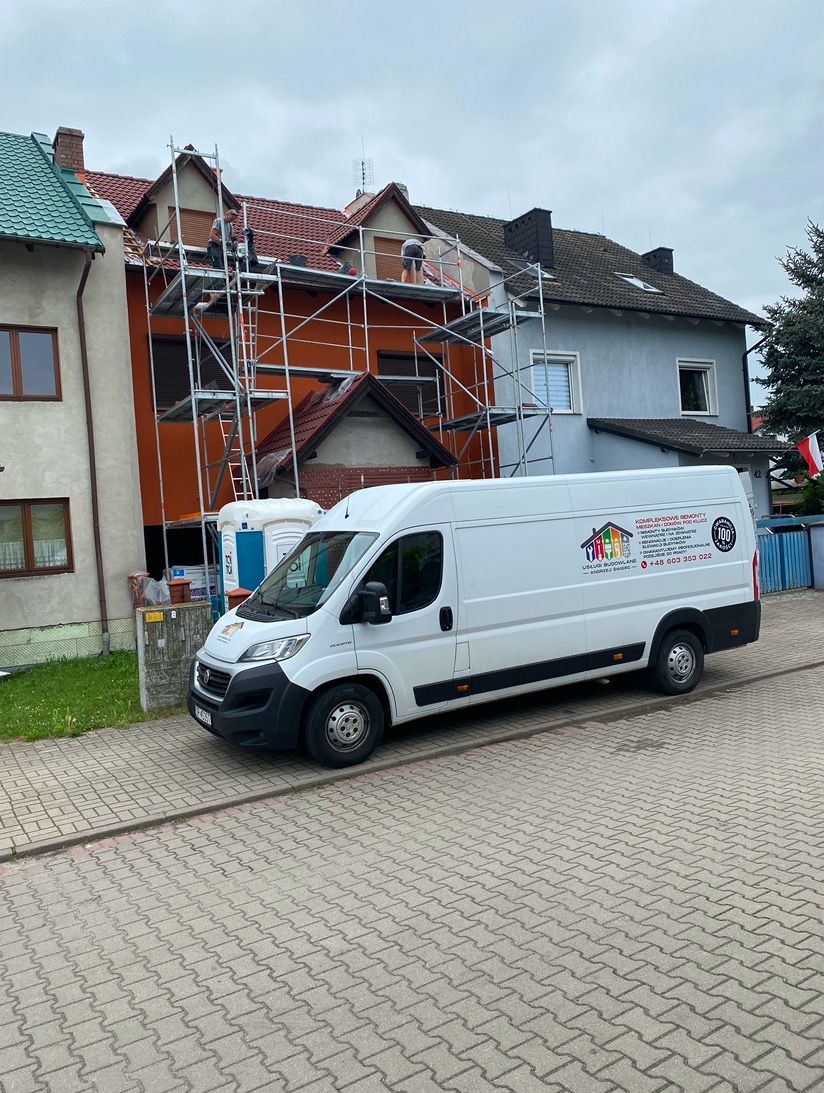 Pracownicy na rusztowaniu podczas renowacji elewacji budynku z pomarańczową fasadą. Na pierwszym planie biały samochód dostawczy z logo firmy.