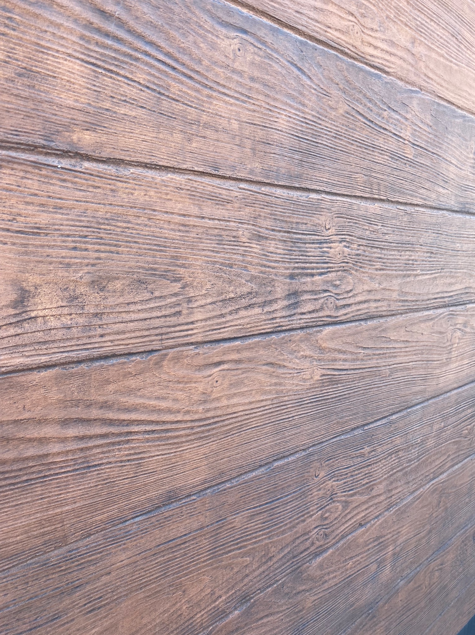 Teksturowana elewacja imitująca drewno, z widocznymi słojami i detalami, wykonana w odcieniach brązu. Ujęcie pod kątem, podkreślające fakturę i wzór.