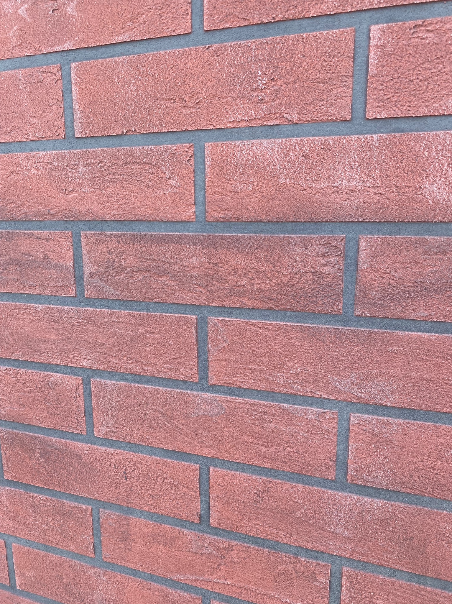 Ceglana ściana z szarą fugą, ułożona pod kątem. Widoczna faktura cegieł i precyzyjne wykonanie spoin. Detal wykończenia elewacji w ciepłej tonacji.