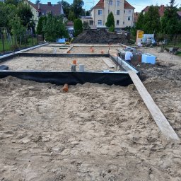 Usługi instalacyjne Michał Smektalski - Fundamenty domu jednorodzinnego w trakcie budowy, widoczne zbrojenia i izolacja, na tle domy i drzewa.