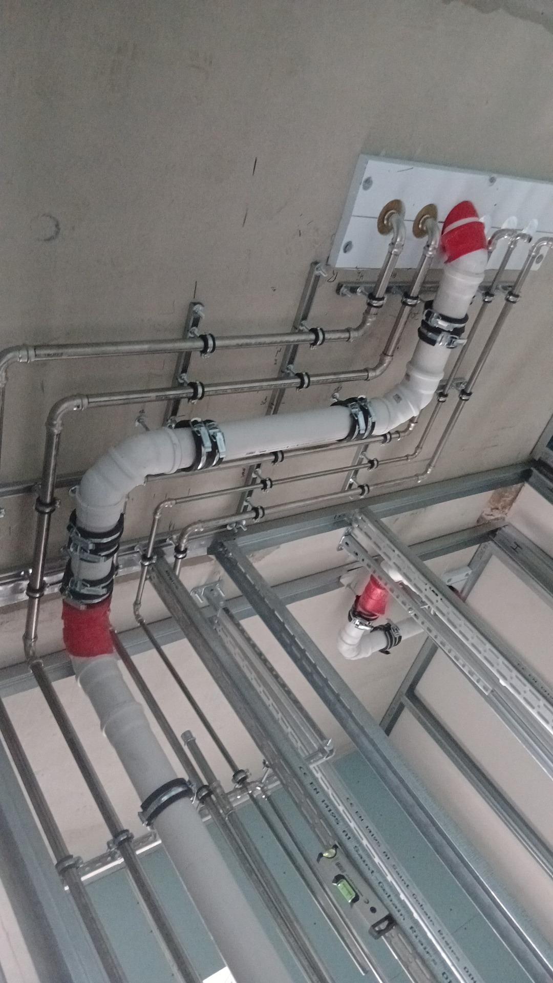 Instalacja rur pod sufitem, widoczne rury metalowe i plastikowe, uchwyty montażowe, fragment stelażu sufitu podwieszanego i zabezpieczenia na końcach rur.