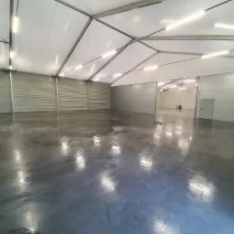 Wnętrze hali magazynowej z betonową posadzką po umyciu, widoczne odbicia świetlówek w mokrej powierzchni.