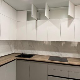 MEBLE NA WYMIAR NV Service - Nowoczesna kuchnia z białymi szafkami górnymi (część otwarta) i szarymi dolnymi, drewniany blat, marmurowa ściana. Minimalistyczny design, oświetlenie sufitowe.