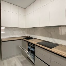 MEBLE NA WYMIAR NV Service - Nowoczesna kuchnia w odcieniach szarości i bieli z drewnianym blatem. Otwarta zmywarka, minimalistyczne szafki górne, marmurowe wykończenie ściany nad blatem.