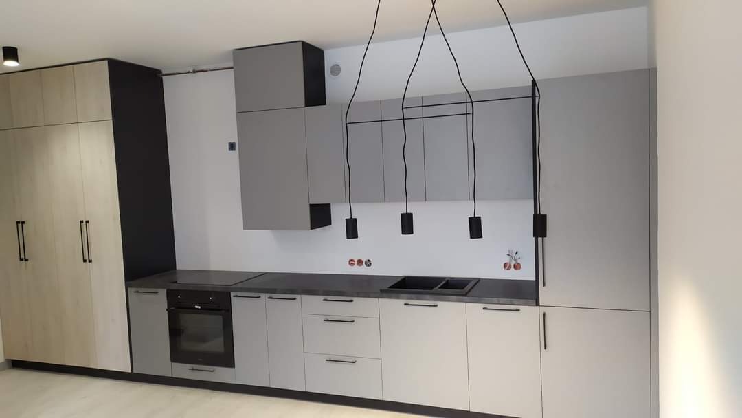 Nowoczesna kuchnia z szarymi i drewnopodobnymi frontami, czarnym blatem i minimalistycznym oświetleniem wiszącym.