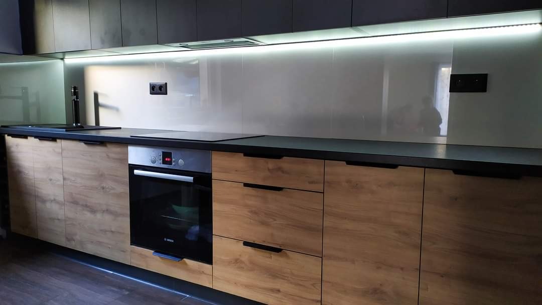 Nowoczesna kuchnia z drewnianymi frontami szafek, czarnym blatem i podświetleniem LED pod górnymi szafkami.