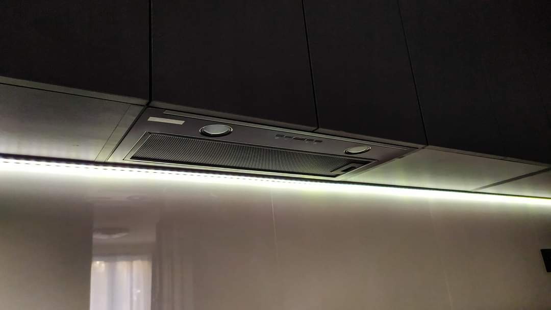 Ciemna zabudowa kuchenna z zamontowanym okapem podszafkowym i oświetleniem LED podszafkowym.