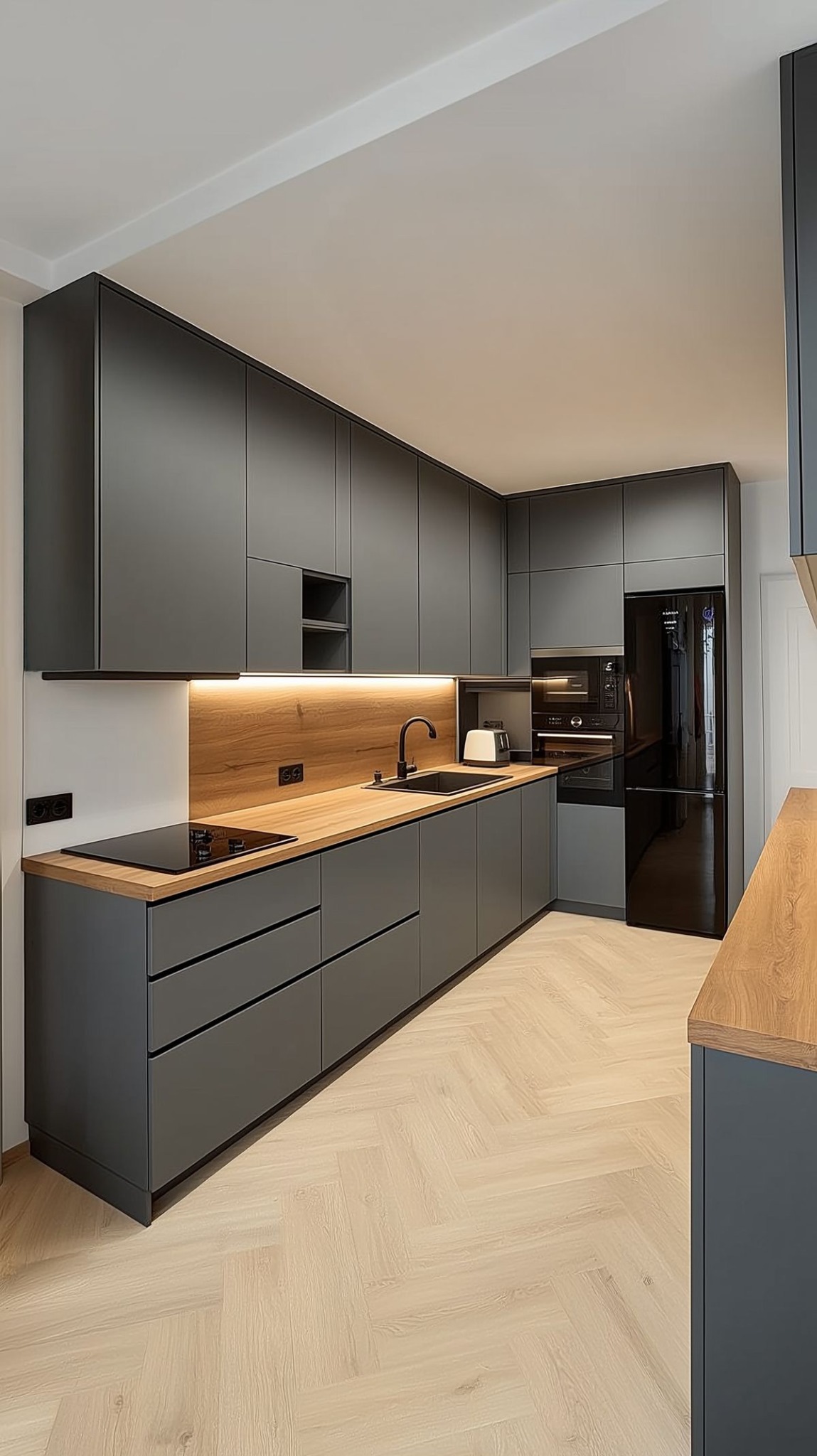 Nowoczesna kuchnia na wymiar z szarymi frontami, drewnianym blatem i oświetleniem LED. Parkiet ułożony w jodełkę. Widoczny czarny sprzęt AGD.